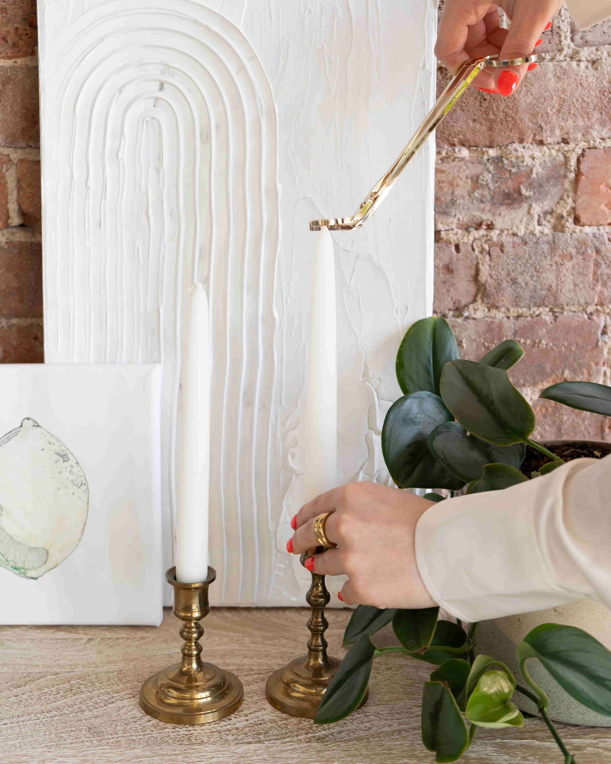 Woman trimming candle wick on 9" white taper candles.