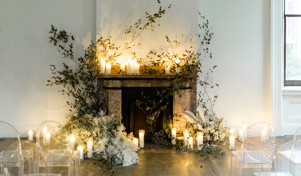 Lit pillar candles on a wedding mantel and floor beneath a trailing greenery installation