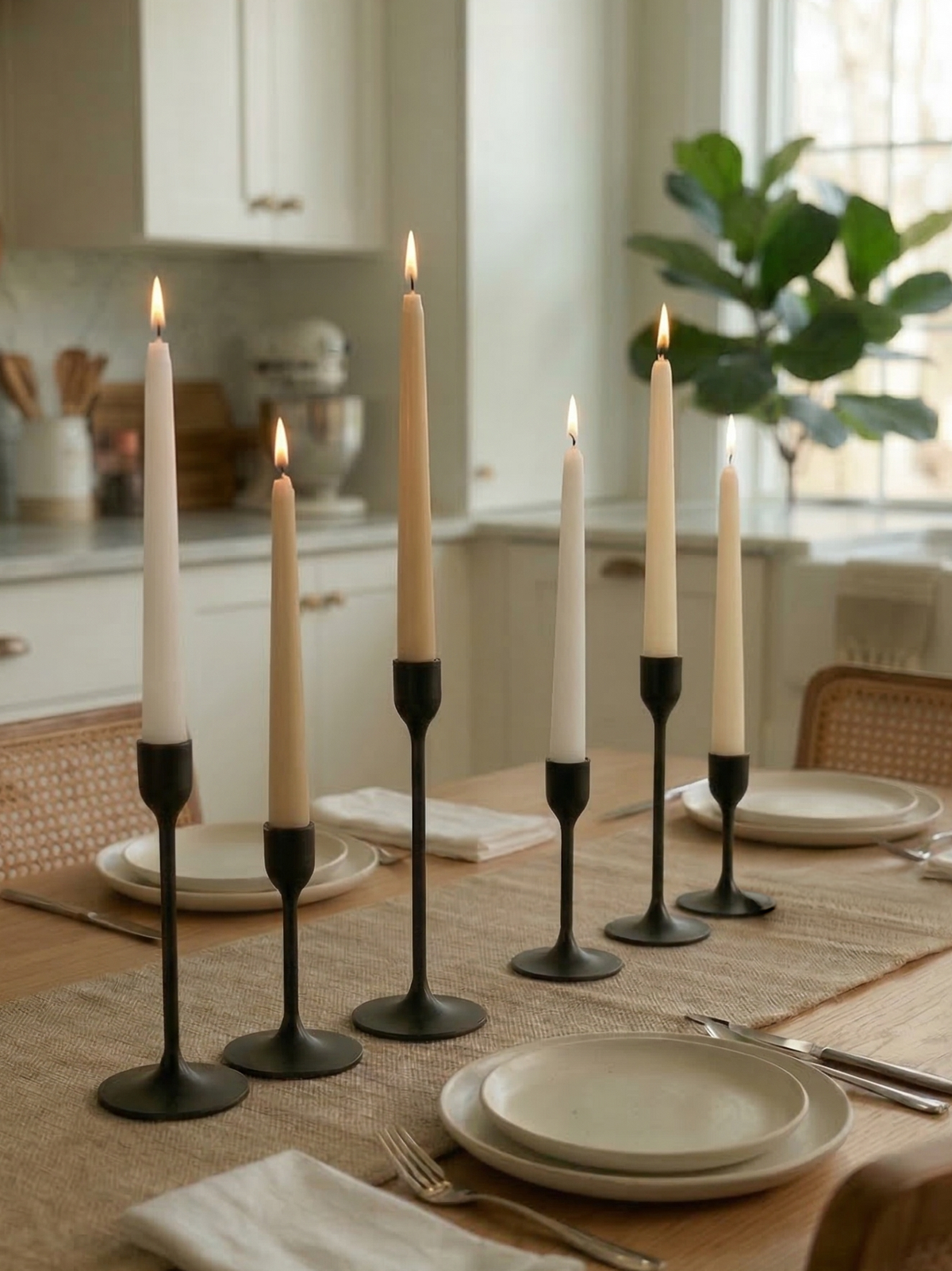Candlelit dining table setting with black candle holders and white candles in a kitchen.