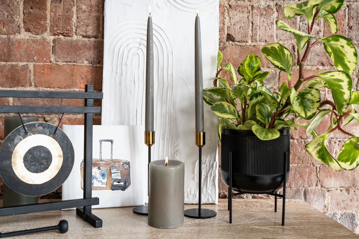 Decorative items including Paris Gray taper candles, a plant, and a gong against a brick wall.