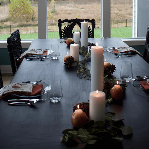 A dark table with white pillar candles of all sizes and  cafe au lait petite pillar candles 