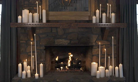 A rustic fireplace decorated with white pillar and taper candles. 