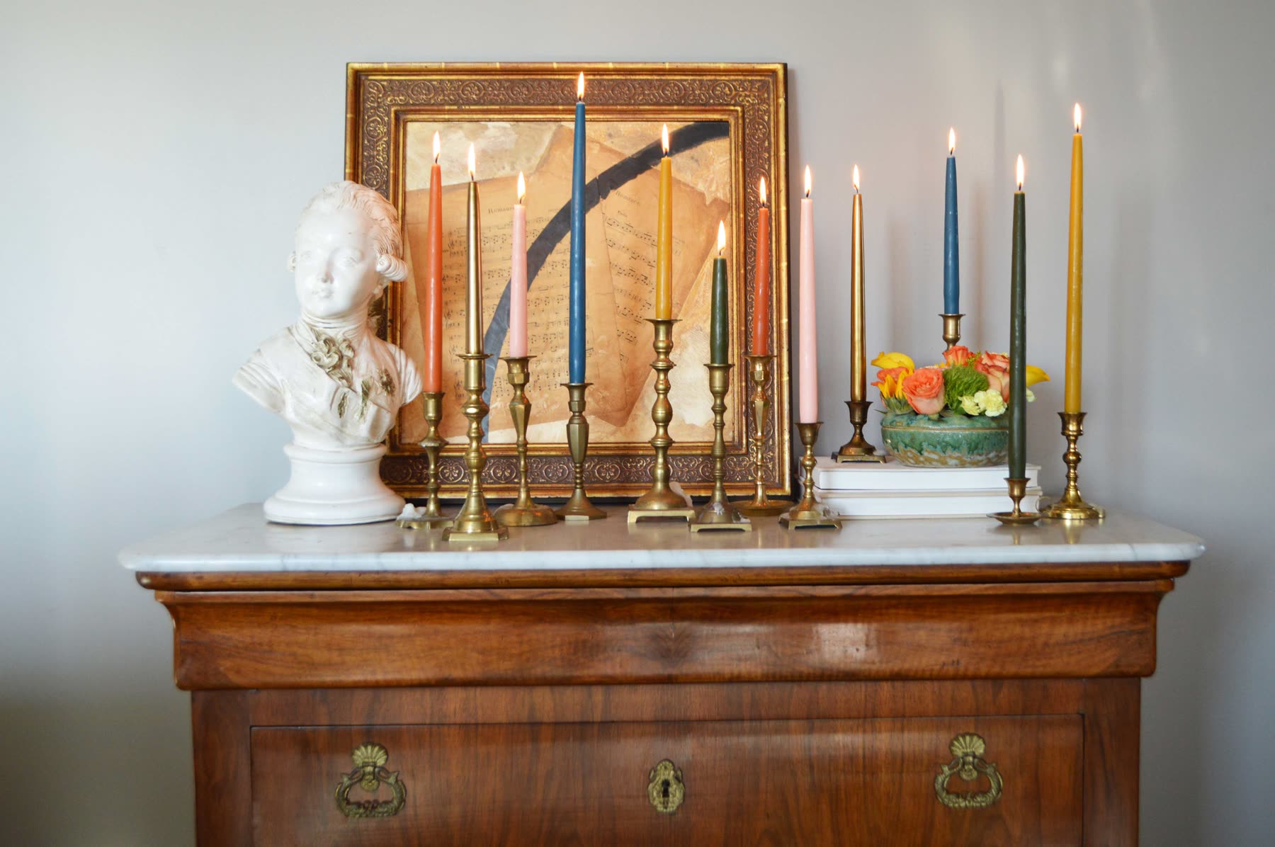 Colorful taper candles arranged on an antique dresser in brass candlesticks